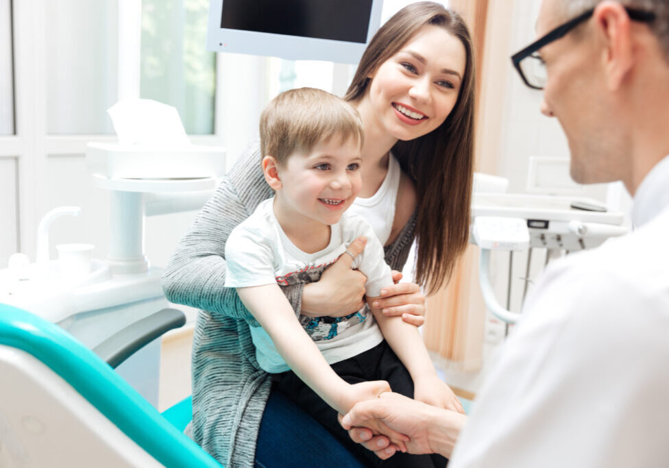 Happy pretty mother and little boy talking to dentist in dental clinic