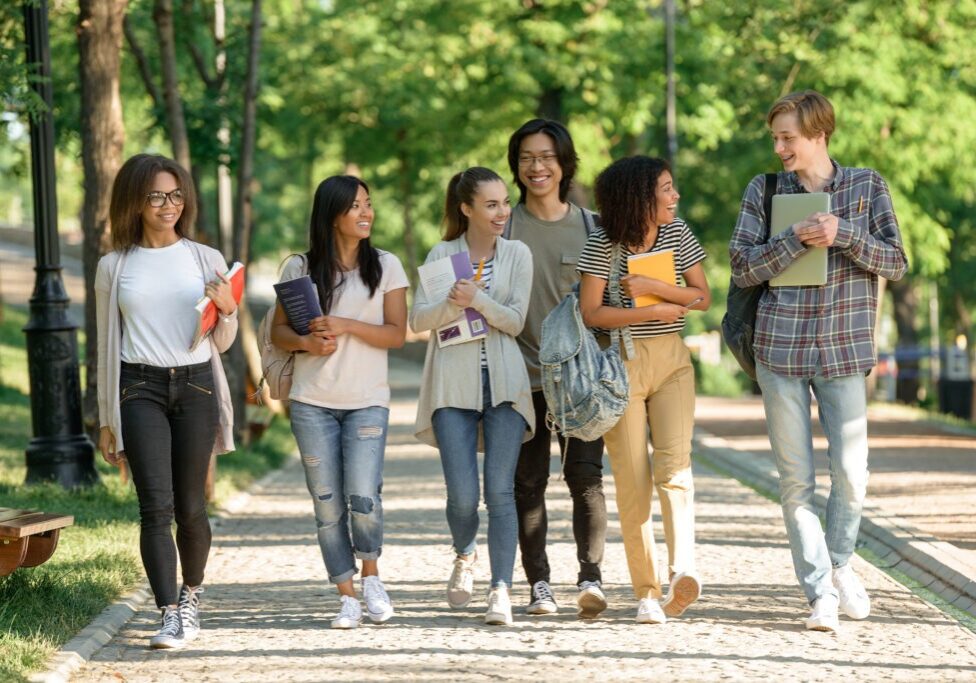 Image of multiethnic group of happy young students walking outdoors. Looking aside.
