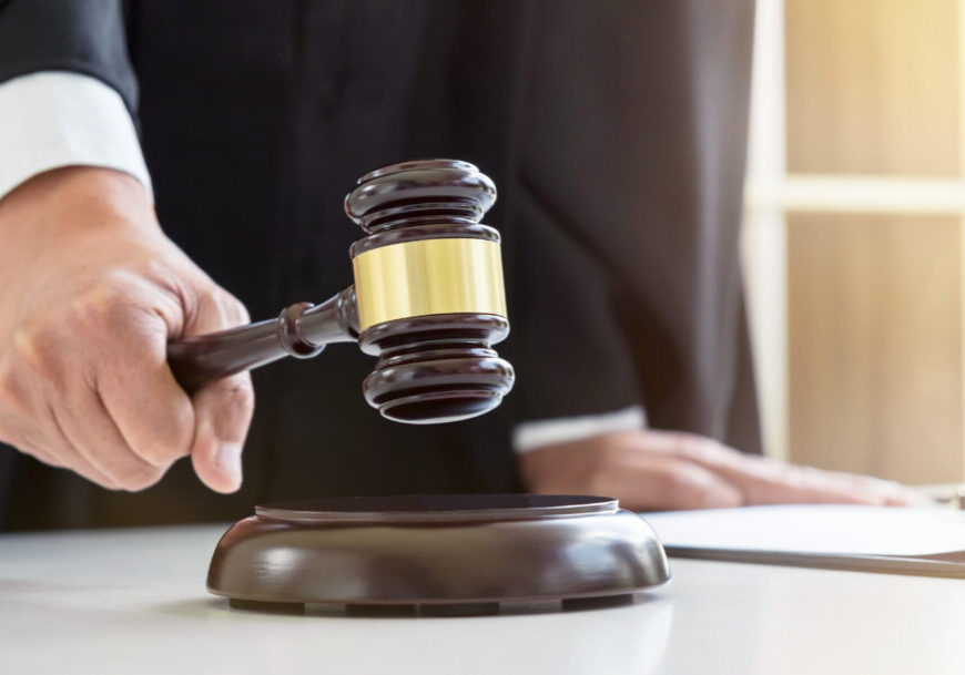 Close up of Male lawyer or judge hand's striking the gavel on sounding block, working with Law books, report the case on table in modern office, Law and justice concept.