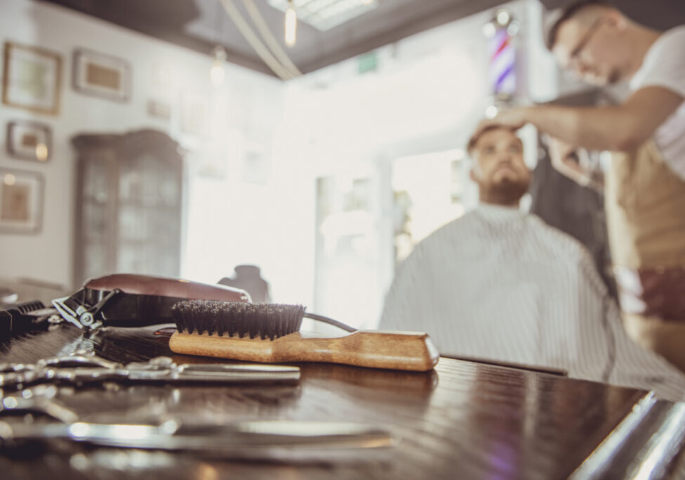 Accesories for cutting on the table in a barbershop and a hairdresser works in the background.  Photo in vintage style