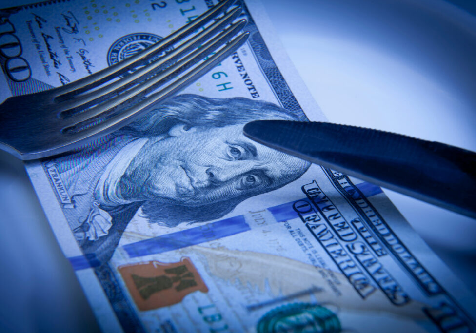 Close up of US Dollar on a plate, fork and knife as a symbol of money hungry. Business, motivation, success concept.
