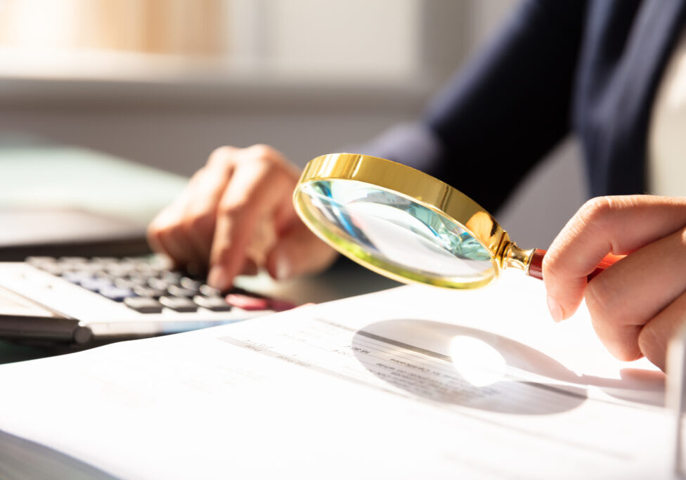 Close-up Of A Businesswoman's Hand Examining Invoice Through Magnifying Glass