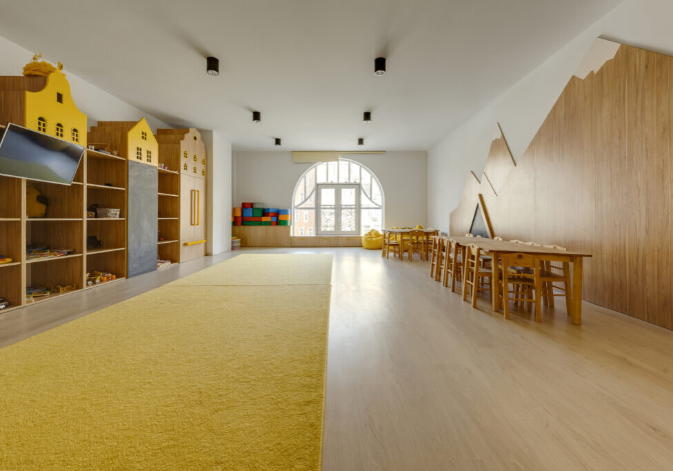 cozy kindergarten classroom interior with yellow carpet, tables and tv
