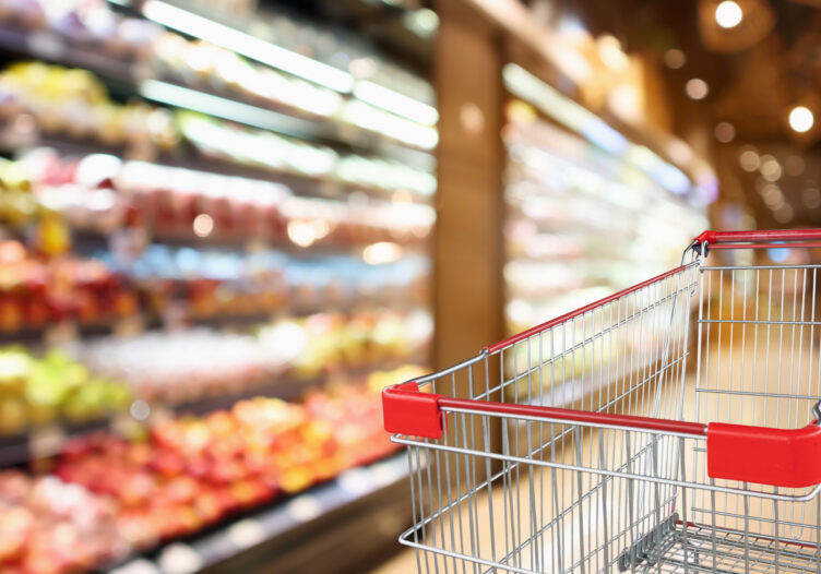supermarket grocery store with fruit and vegetable shelves interior defocused background with empty red shopping cart