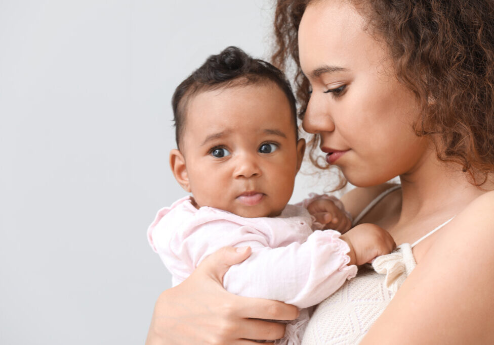 African-American woman with cute little baby on light background