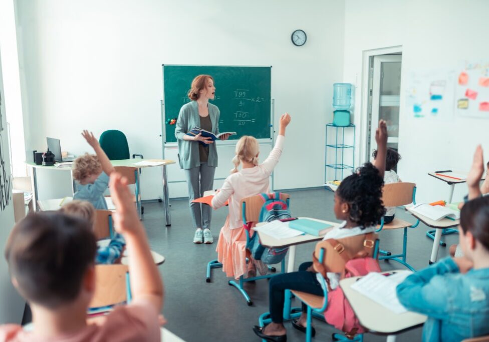 Doing sums. Young maths teacher standing in front of the class and calling one of pupils to the blackboard.