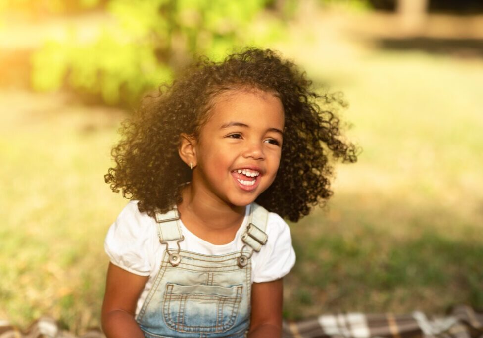 Happy african-american girl sitting on blanket and laughing, walking in park, free space