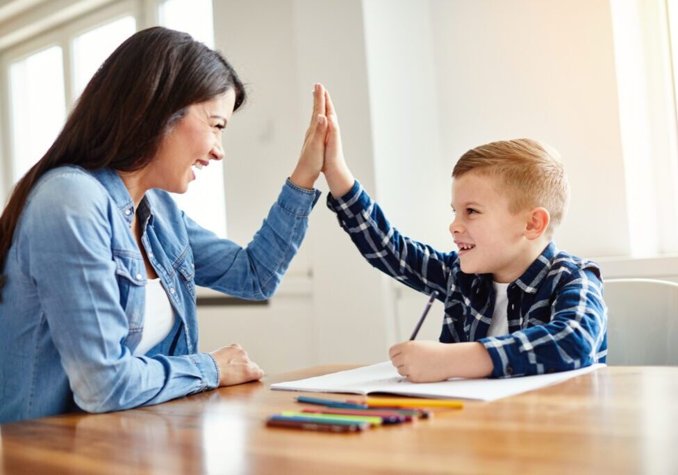 mother teaching son and helping with homework at home, son giving high five to mother