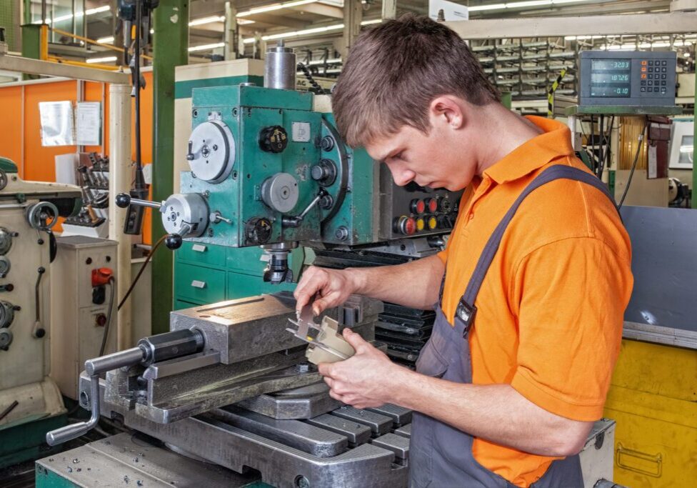 A trainee in the metalworking industry checks a workpiece using a caliper