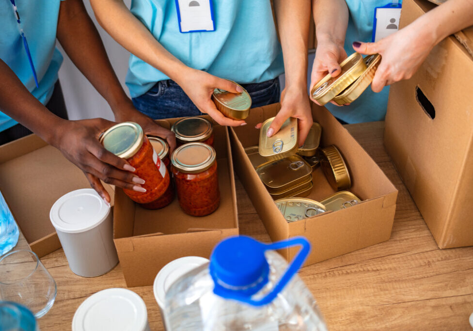 Small mixed race group of people working in charitable foundation. Generous people helping to poor people. People Donating Food To Charity Food Bank Collection In Community Center