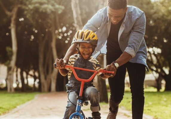 Boy learning to ride a bicycle with his father in park. Father teaching his son cycling at park.