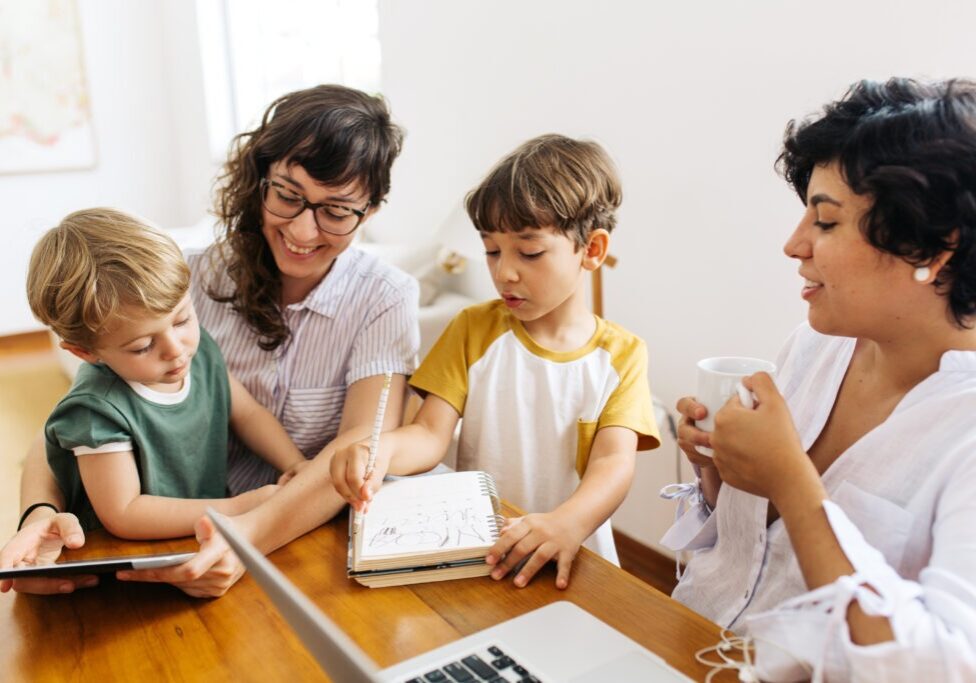 Happy LGBT family at home. Lesbian couple sitting with their kids using a digital tablet.