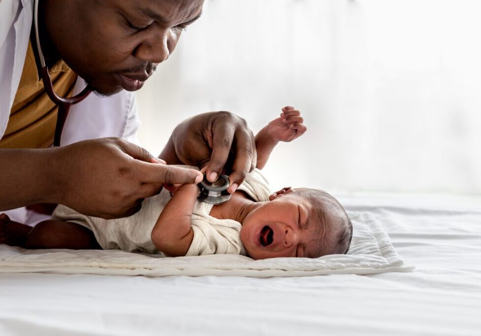 African doctor using a stethoscope, checking the respiratory system and heartbeat Of a 12-day-old baby black skin newborn, which laying and crying on the bed, to baby black skin newborn and  health care concept.