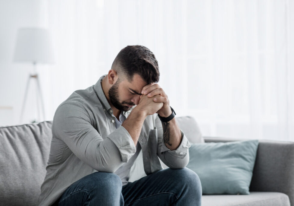 Unhappy depressed caucasian male crying, covering face in living room on couch, feeling desperate and lonely, isolated at home. Stressed from work, unemployment, anxiety, heartbroken and depression