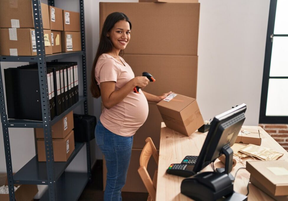 Young latin woman pregnant business worker scanning package label at office