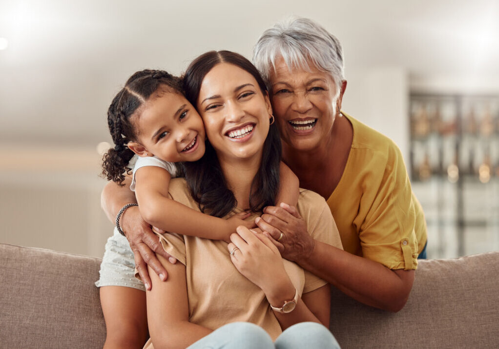 Grandmother, mom and child hug in a portrait for mothers day on a house sofa as a happy family in Colombia. Smile, mama and elderly woman love hugging young girl or kid and enjoying quality time.