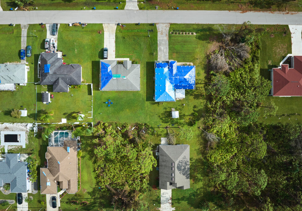 Aerial view of damaged in hurricane Ian house roofs covered with blue protective tarp against rain water leaking until replacement of asphalt shingles.