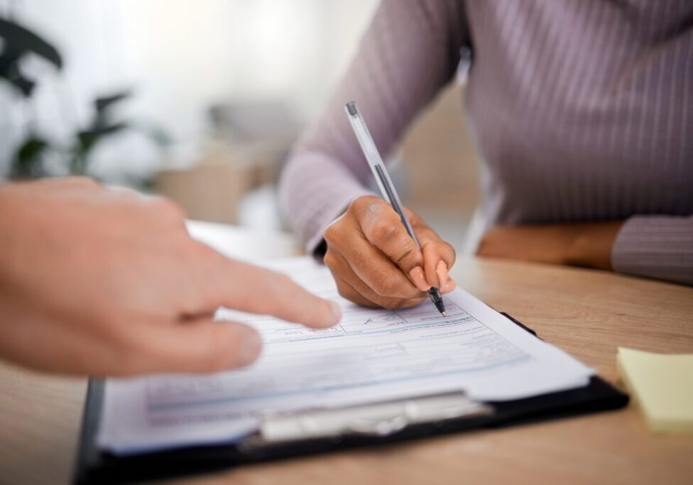 Healthcare, documents and writing with a patient hand using a pen in a doctor office for insurance information. Hospital, paper or contract with a black woman signing a form during medical consulting.