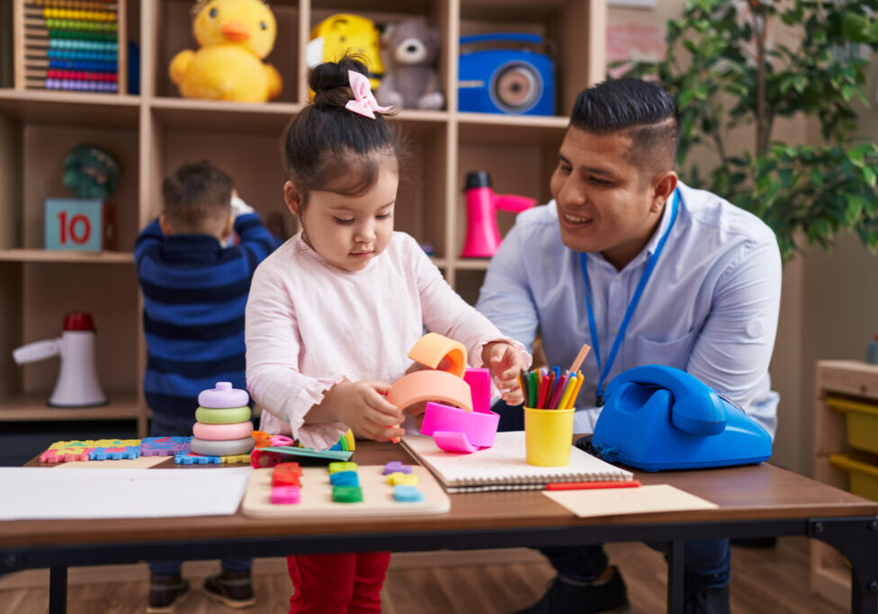 Hispanic man with boy and girl playing with construction blocks sitting on table at kindergarten