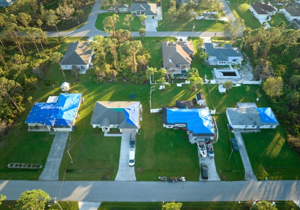 Hurricane Ian damaged house rooftops covered with protective plastic tarp against rain water leaking until replacement of asphalt shingles. Aftermath of natural disaster.